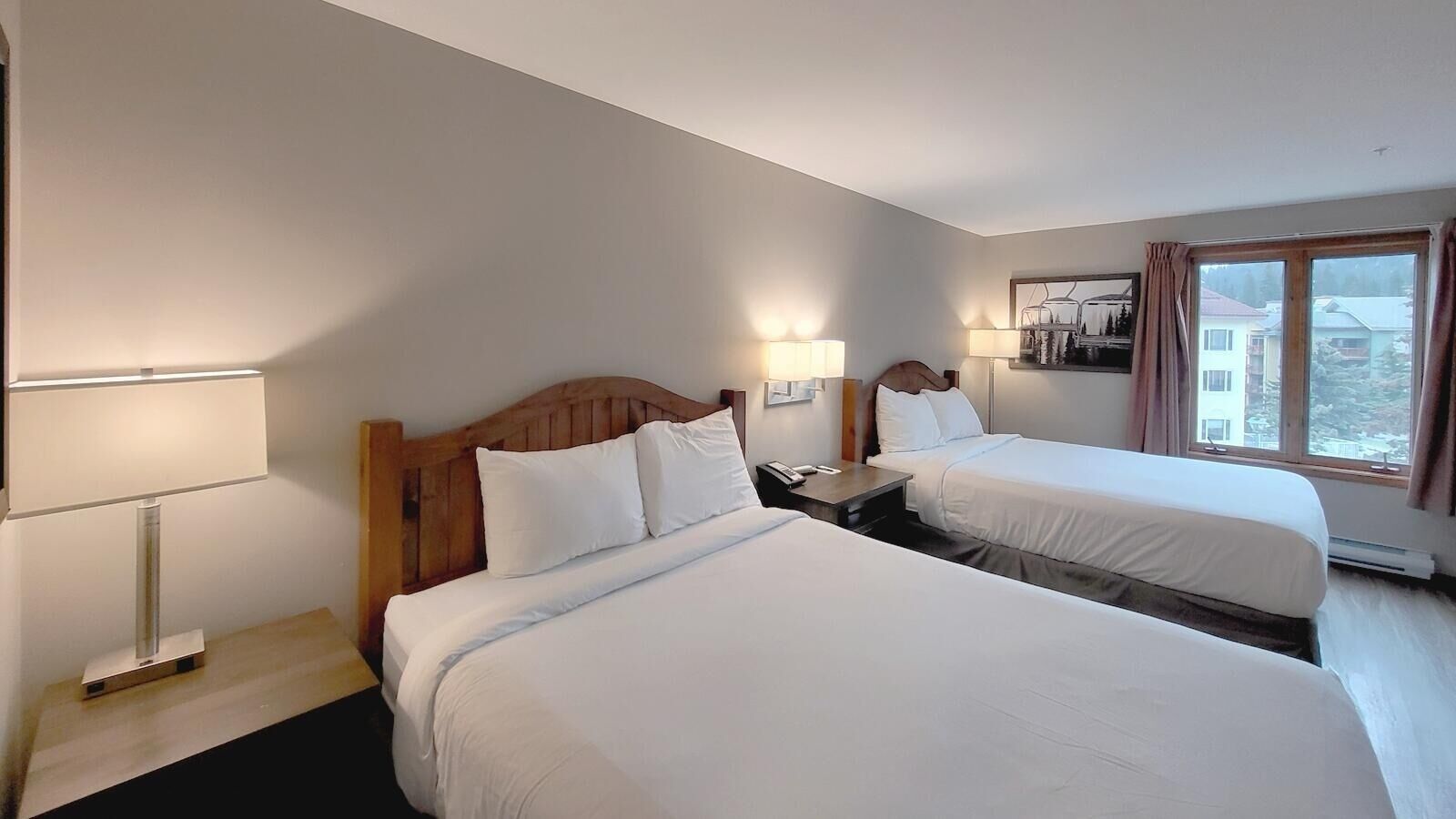 Una habitación de hotel con dos camas, una mesita de noche, una lámpara y una ventana con cortinas.