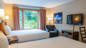 A hotel room with two beds, a TV, a chair, and a desk with a lamp.