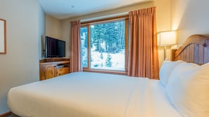 A hotel room with a large bed, a TV on a wooden cabinet, and a window with curtains.