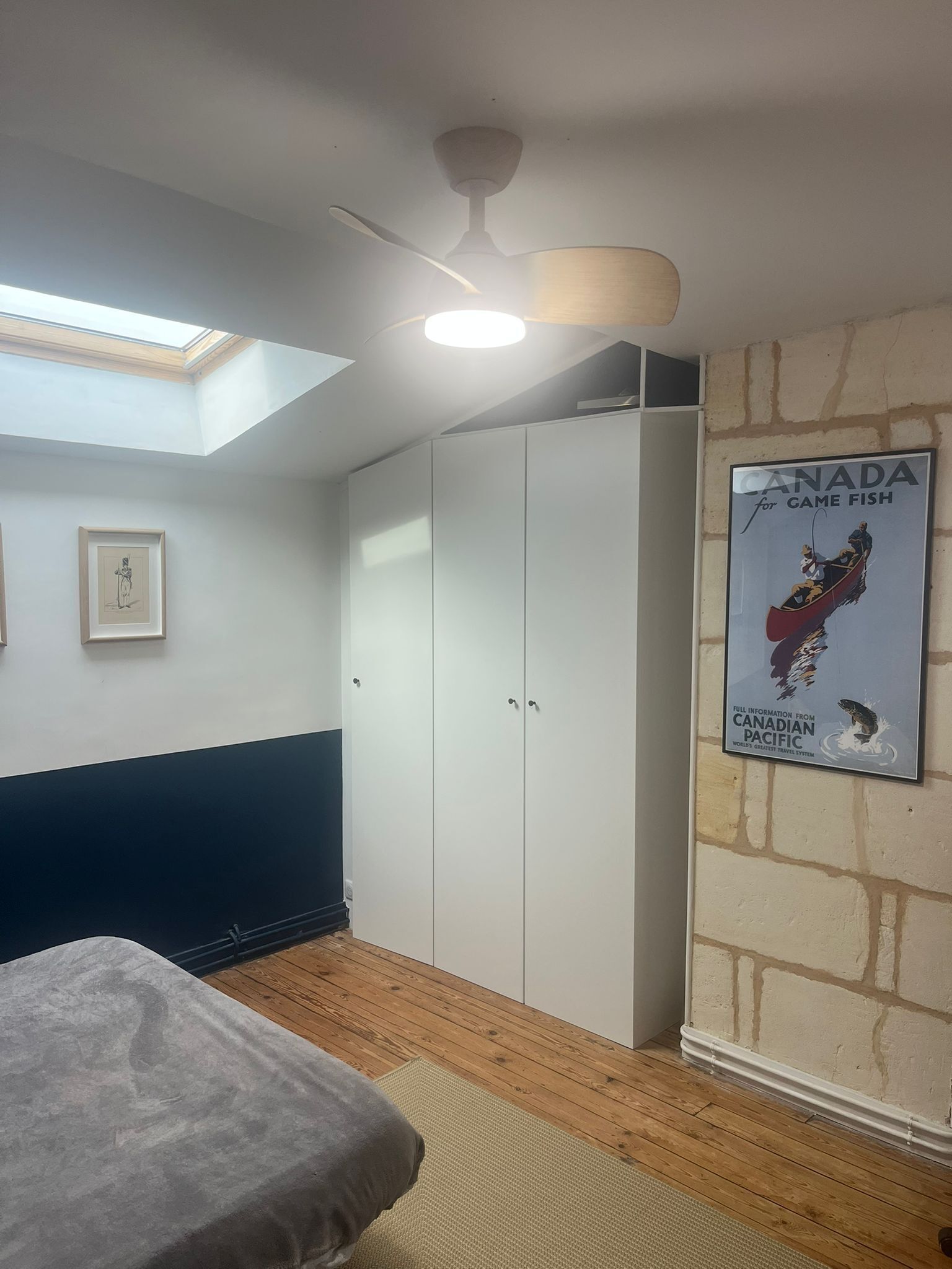 Un dormitorio con tragaluz, ventilador de techo, cama, armario y un cartel en la pared.