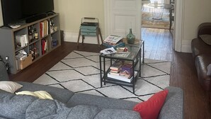 En stue med en grå sofa, et sofabord, en reol, et fjernsyn og en dør til et udendørs område.