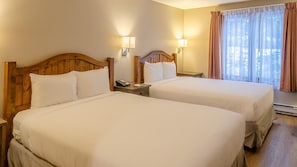 Een hotelkamer met twee bedden, houten hoofdeinden, bedlampjes, een telefoon en een raam met gordijnen.