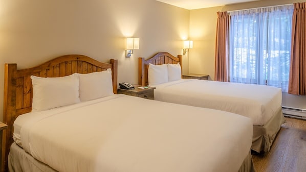 Habitación de hotel con dos camas, cabeceros de madera, lámparas de noche, un teléfono y una ventana con cortinas.
