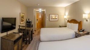 A hotel room with two beds, a desk with a TV, a coffee machine, and a door leading to another room.
