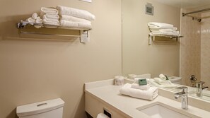 Un baño moderno con inodoro, lavamanos y ducha. Hay varias toallas blancas en estantes y encimera.