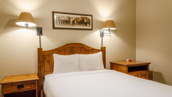Uma cama bem arrumada com cabeceira de madeira, duas mesas de cabeceira com abajures e uma fotografia emoldurada na parede.