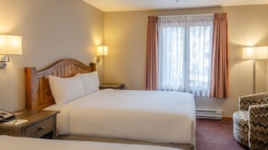 A hotel room with a wooden headboard bed, two bedside tables, a chair, and a window with curtains. - Cahilty #254 Hotel Room (Sun Peaks)
