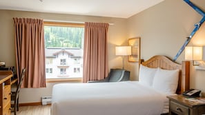 A hotel room with a bed, bedside table, lamp, and a view of a building through the window.