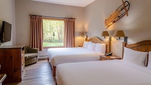 A hotel room with two beds, a wooden headboard, a desk with a chair, a TV, and a window with curtains.