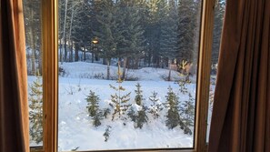A window view of a snowy forest with trees and a lamp post.