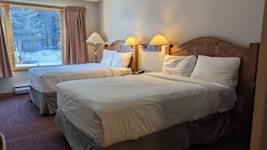 A hotel room with two beds, a window with curtains, and bedside lamps.