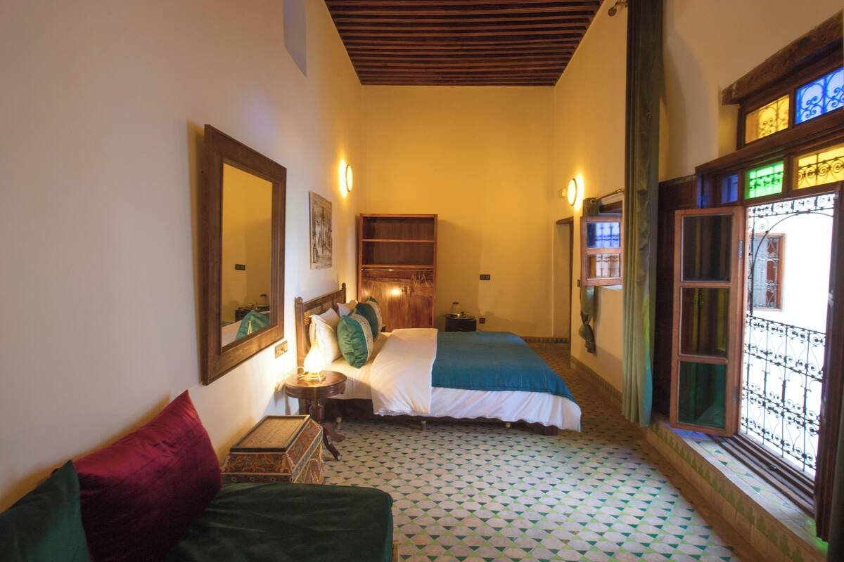Habitación de hotel con cama, mesita de noche, espejo y ventana con vistas.