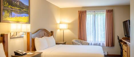 A hotel room with two beds, a desk with a lamp, a TV, and a painting of a mountain landscape.