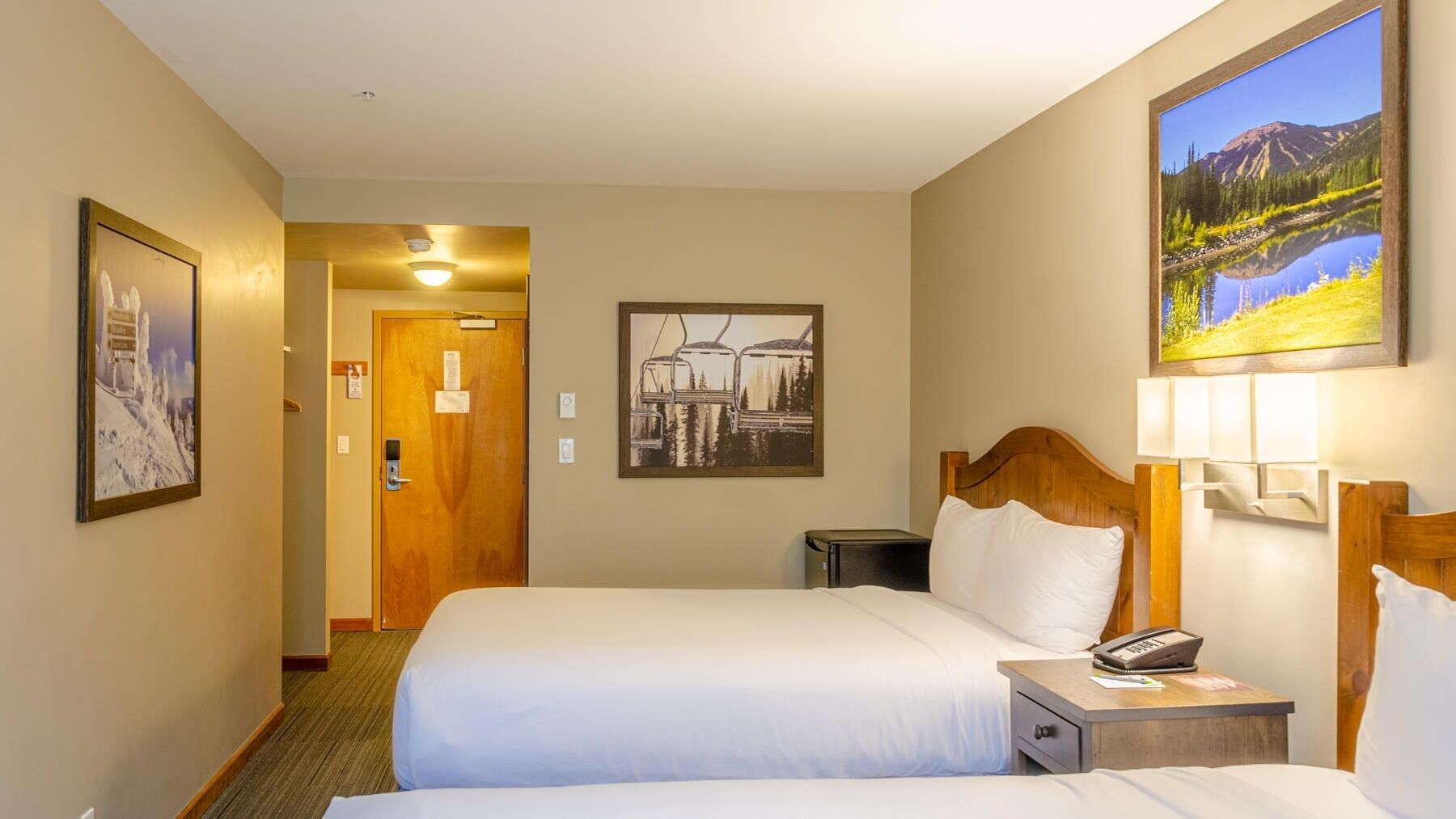 A hotel room with a bed, bedside table, and a painting of a mountain landscape.