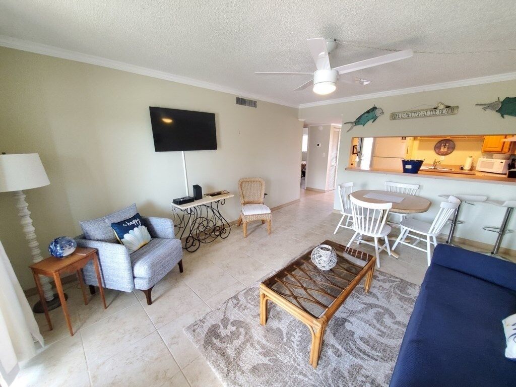 A living room with a sofa, armchair, coffee table, TV, and a dining area with chairs and a table.