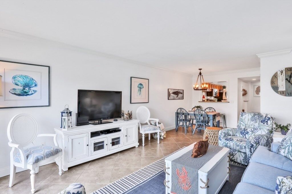 A living room with a TV, white furniture, and a dining area with chairs and a table.