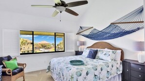 A bedroom with a bed, a hammock, a chair, and a window with a view. - Summerhouse 147 2 Bedroom Condo (St. Augustine)