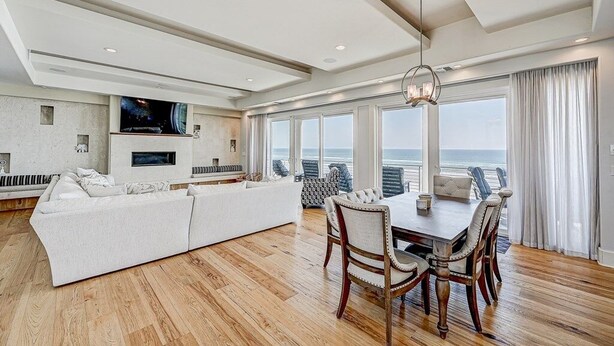 A spacious living room with a large white sofa, a dining table with chairs, and a TV mounted on the wall. - Ocean Paradise 4 Bedroom Home (St. Augustine)