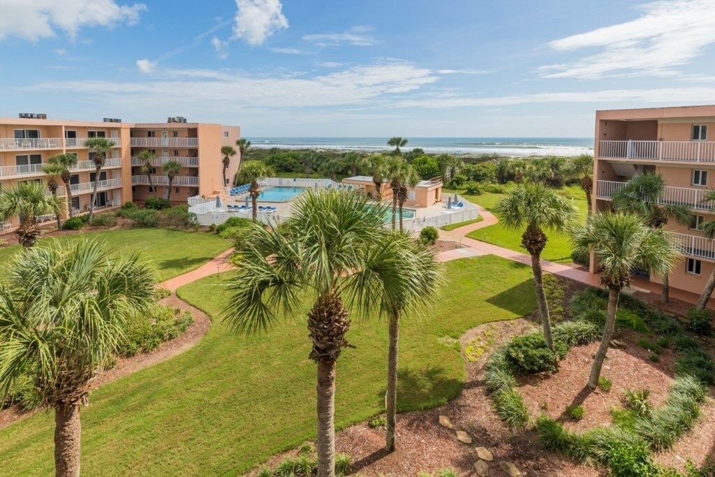 A resort with a pool, palm trees, and a view of the ocean.