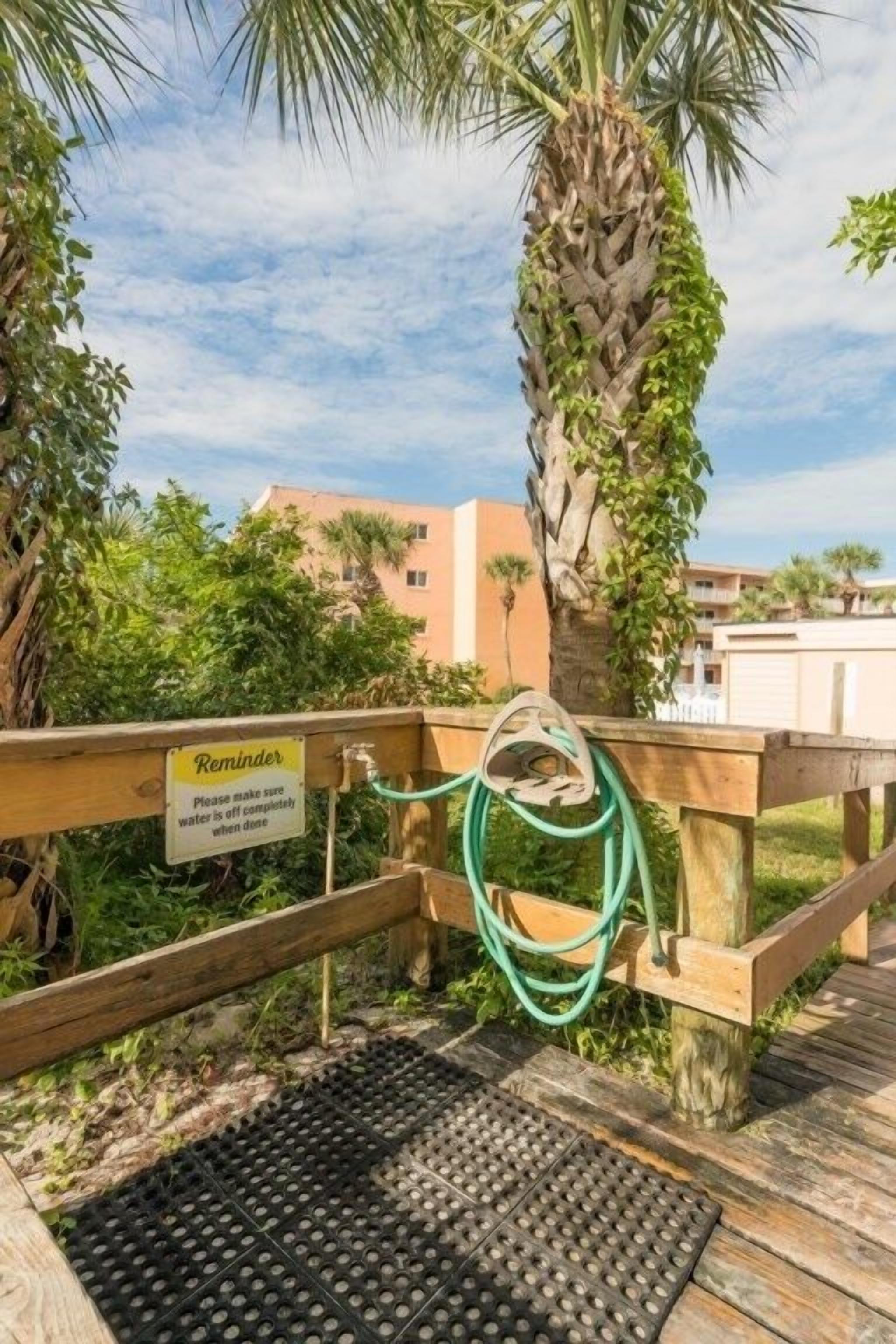 A wooden deck with a sign reminding to turn off water, a green garden hose, and a palm tree.