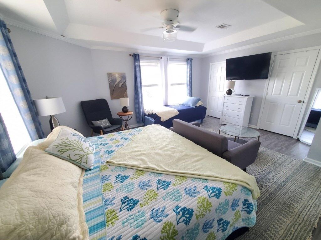 A hotel room with a large bed, a desk, a chair, a TV, and a door.