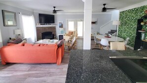 A modern living room with a sofa, a flat-screen TV, and a fireplace. There is a dining area with a table and chairs, and a kitchen with a granite countertop. - All Decked Out - 4 Beds, Pool & Pets Welcome 4 Bedroom Home (St. Augustine)