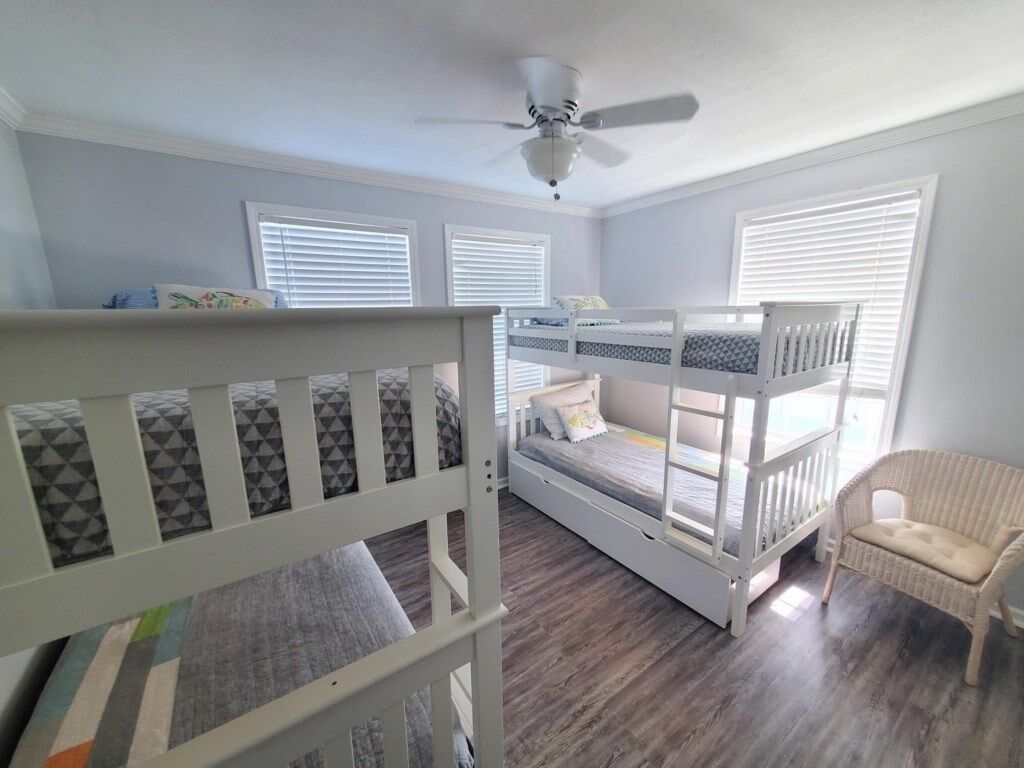 A child's room with bunk beds, a ceiling fan, and a wicker chair.