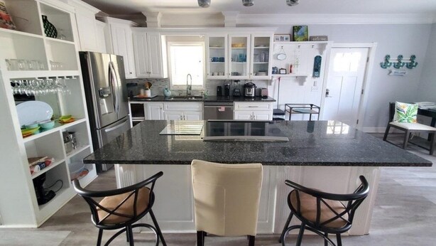 A modern kitchen with white cabinets, a black granite island, and two bar stools. - All Decked Out - 4 Beds, Pool & Pets Welcome 4 Bedroom Home (St. Augustine)