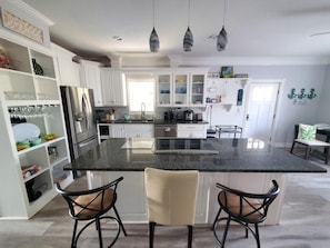 A modern kitchen with white cabinets, a black granite island, and two bar stools. - All Decked Out - 4 Beds, Pool & Pets Welcome 4 Bedroom Home (St. Augustine)
