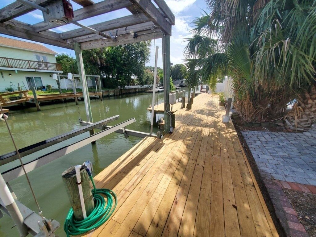 A wooden dock extending into a body of water, with a covered area overhead and a paved walkway beside it.