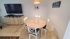 A dining area with a round table, white chairs, a television, and a cabinet. - Zen Cottage - All 4 Bedroom Home (St. Augustine)