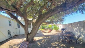 A patio area with a swing set, a round table with chairs, and a large tree providing shade. - Zen Cottage - All 4 Bedroom Home (St. Augustine)