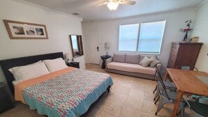 A bedroom with a bed, a sofa, a dining table, and a ceiling fan. - Charming Beach Studio With Wifi & Beach Access 1 Bedroom Home (St. Augustine)
