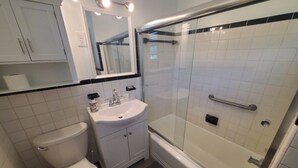 A bathroom with a toilet, sink, mirror, and glass-enclosed shower. - Charming Beach Studio With Wifi & Beach Access 1 Bedroom Home (St. Augustine)