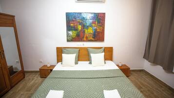 A bedroom with a bed, a nightstand, a mirror, an air conditioner, and a painting on the wall.