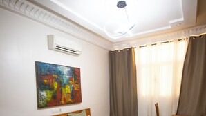 Un dormitorio con cama de madera, escritorio, silla, aire acondicionado y un cuadro abstracto colorido en la pared.