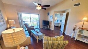A spacious living area with a ceiling fan, a television, a sofa, and a dining table. - Ocean Village Club I35: Pool & Ocean Views 2 Bedroom Condo (St. Augustine)