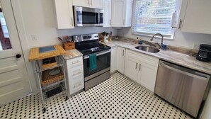 A compact kitchen with white cabinets, a stainless steel microwave, a stove, and a dishwasher. - Downtown Getaway - Pet Friendly 3 Bedroom Home (St. Augustine)