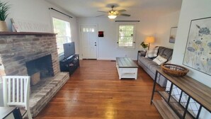 A living room with a fireplace, a ceiling fan, a sofa, and a coffee table. - Downtown Getaway - Pet Friendly 3 Bedroom Home (St. Augustine)