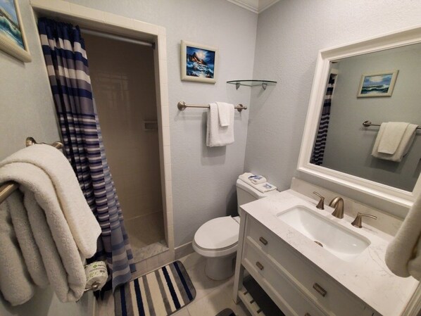 Een badkamer met toilet, wastafel en douche. Handdoeken hangen aan de muur en er ligt een gestreept kleed op de vloer.