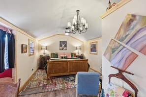 A bedroom with a wooden bed, a chandelier, a patterned rug, and artwork on the walls. - Blitzen - Reindeer Ranch At Round Top Cabin (Ledbetter)