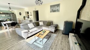 A modern living room with a grey sectional sofa, a wooden coffee table, and a dining area with a table and chairs. - Le refuge | Garden | Wifi | Parking | Near Limoges (Le Palais-sur-Vienne)