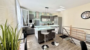 A modern kitchen with a central island, stainless steel appliances, and a dining area with bar stools. - Le refuge | Garden | Wifi | Parking | Near Limoges (Le Palais-sur-Vienne)
