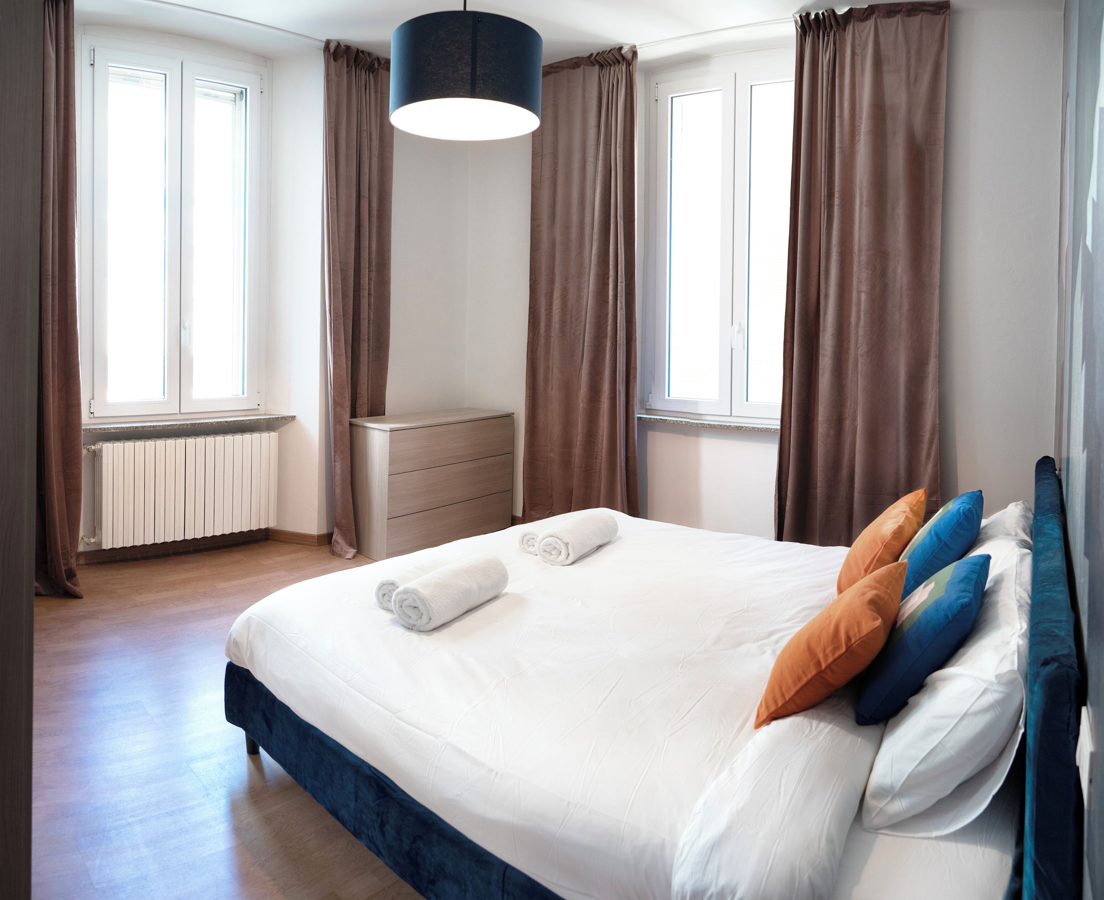 Un dormitorio con cama, mesita de noche, radiador y cortinas.