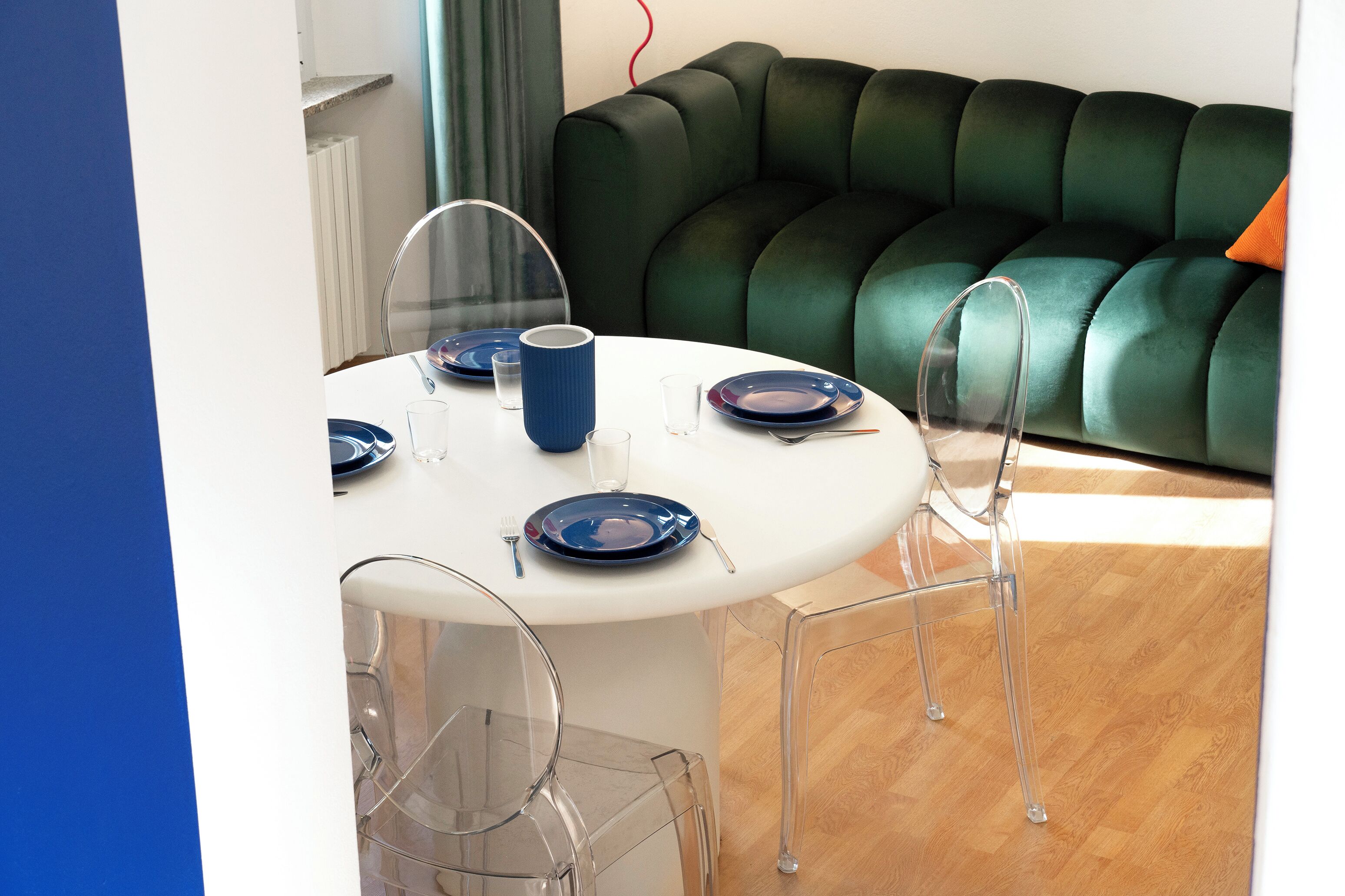 A dining area with a white table, clear chairs, and a green sofa in the background.