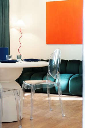 A modern room with a clear plastic chair, a white table with blue plates, a lamp, and a green couch. - MetaphysiComo (Como)