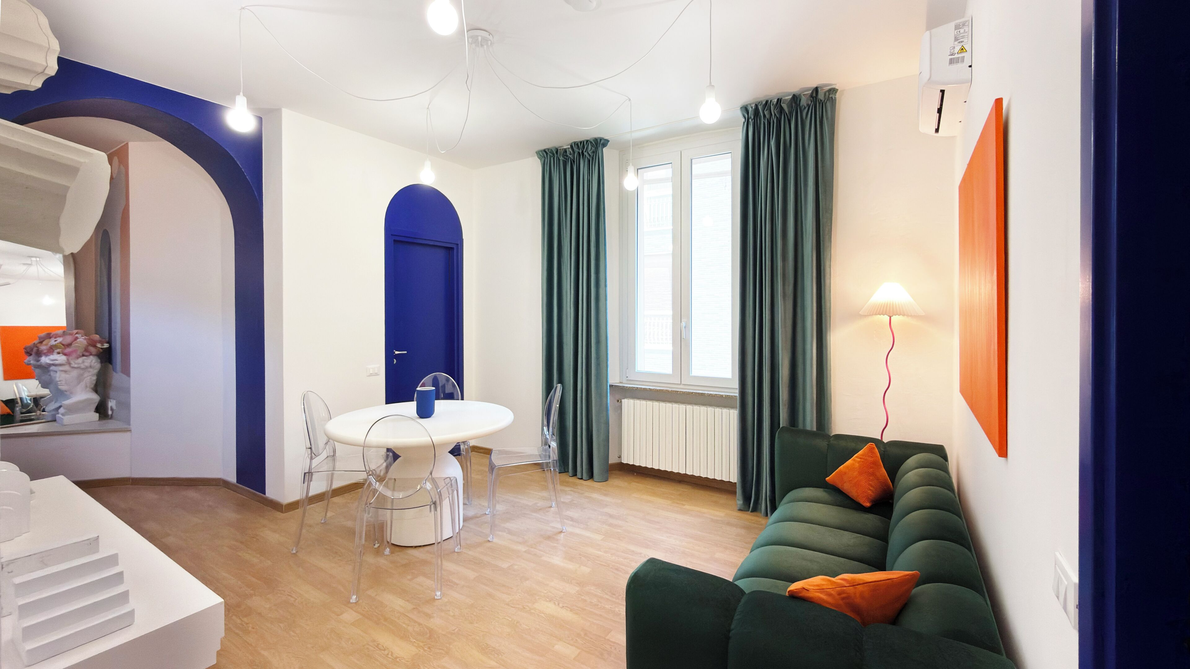 Un salon moderne avec un canapé vert, une table à manger avec des chaises, une porte bleue et une fenêtre avec des rideaux.