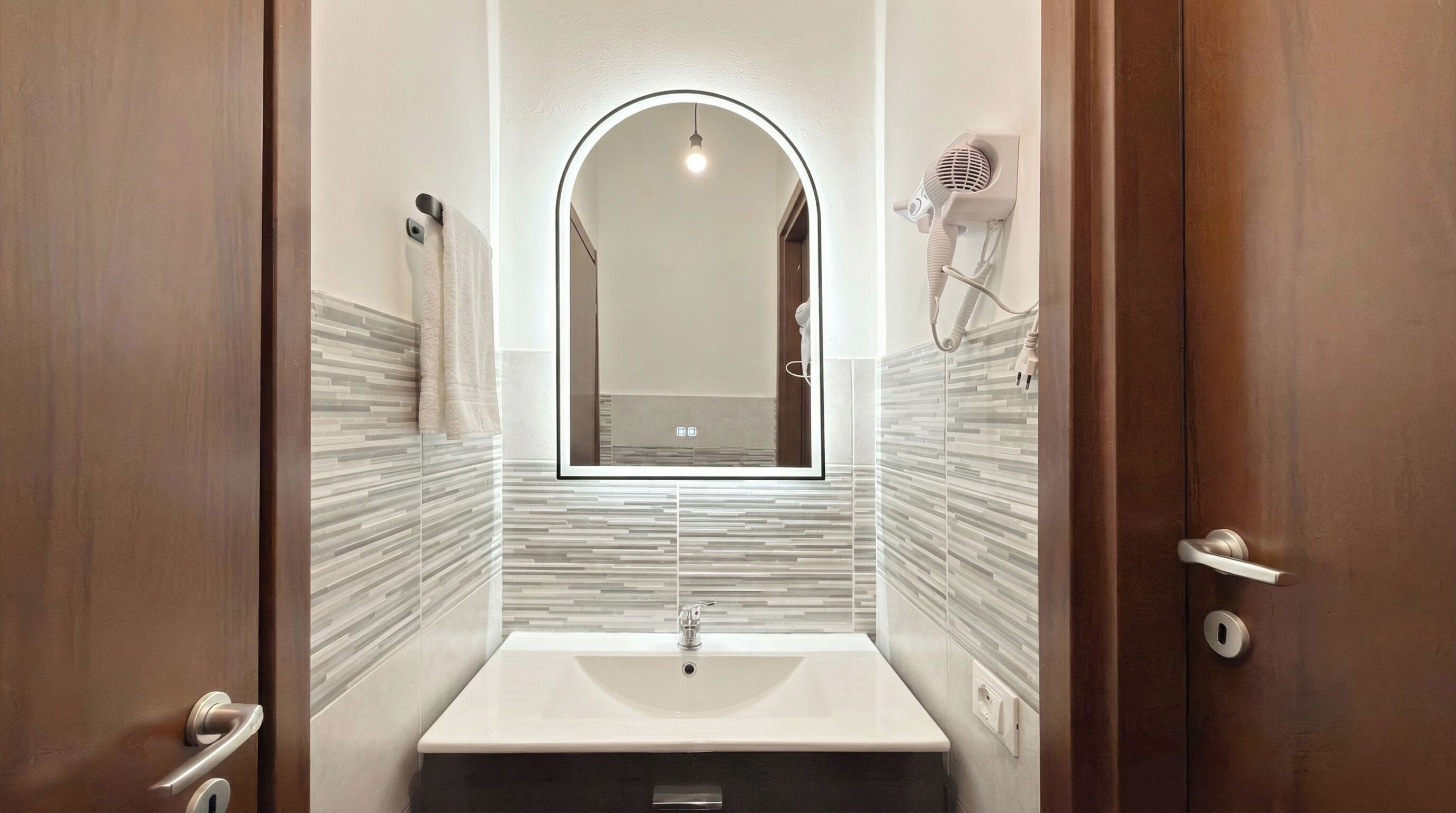 Un baño con un lavamanos rectangular, un espejo con luz y un perchero para toallas.