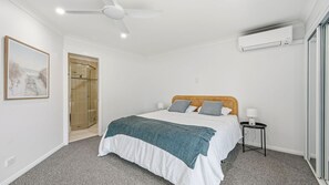 A bedroom with a bed, a nightstand, a wall-mounted air conditioner, a ceiling fan, and a door leading to a shower area. - Flynns Beach Retreat, 3 of 3 Everard street (Port Macquarie)