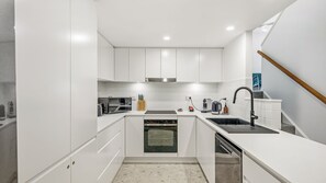 A modern kitchen with white cabinetry, a stainless steel range hood, a built-in oven, a dishwasher, and a sink with a black faucet. - Flynns Beach Retreat, 3 of 3 Everard street (Port Macquarie)